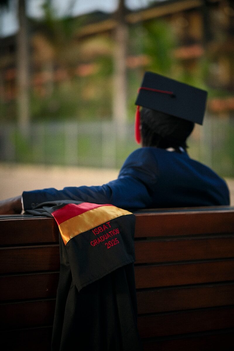 Person in graduation cap and gown on bench.